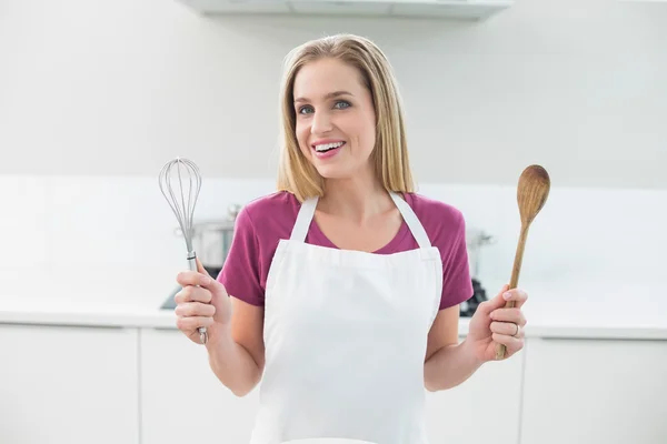 Casual cheerful blonde showing wooden spoon and whisk — Stock Photo, Image