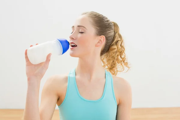 Calm slim blonde sitting on floor drinking from sports bottle — Stock Photo, Image