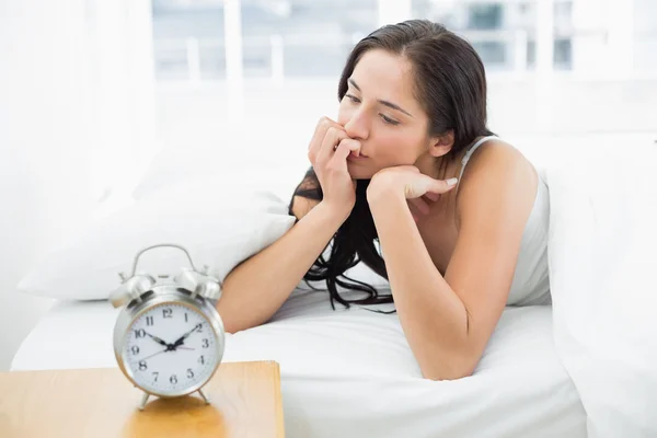 Tankeväckande kvinna i sängen med väckarklocka i förgrunden — Stockfoto