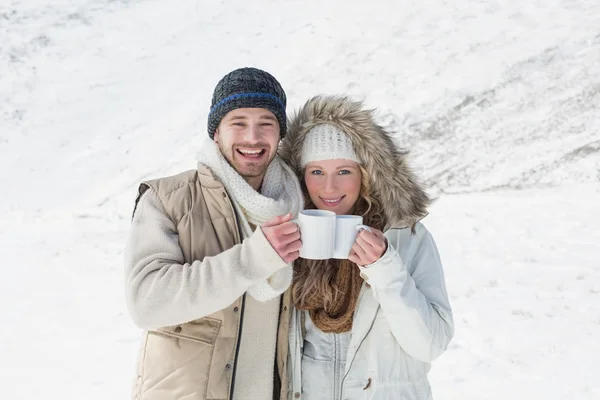 Paar in warmer Kleidung mit Kaffeetassen auf verschneiter Landschaft — Stockfoto