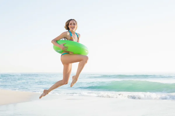 Pretty young woman holding a rubber ring while jumping on beach — Stock Photo, Image