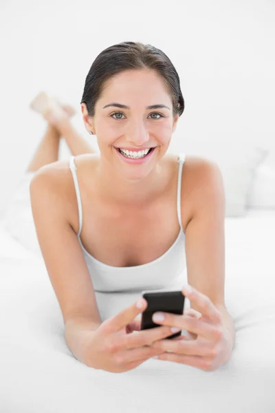 Retrato de uma mulher sorridente com telefone celular na cama — Fotografia de Stock