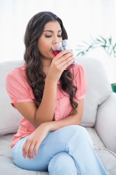 Spokojny, ładny brunetka siedzi na kanapie do picia szklanka soku — Zdjęcie stockowe