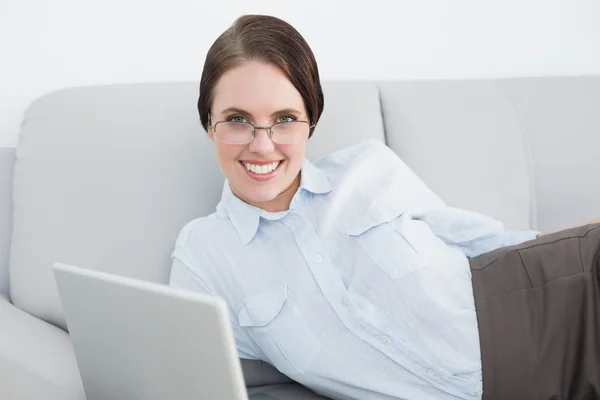 Inteligentemente vestido mulher sorridente com laptop no sofá — Fotografia de Stock