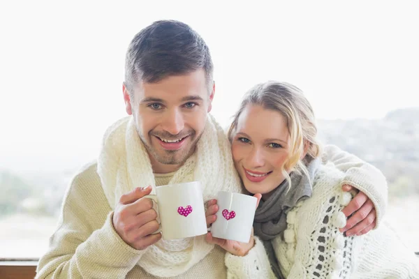 Casal amoroso em roupas de inverno com xícaras de café contra janela — Fotografia de Stock