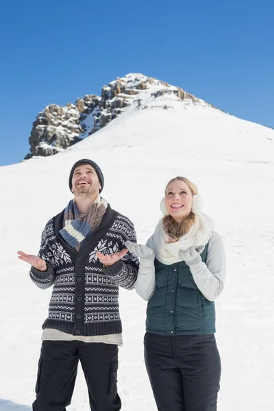 Pareja con las manos abiertas mirando hacia arriba frente a la colina nevada — Foto de Stock