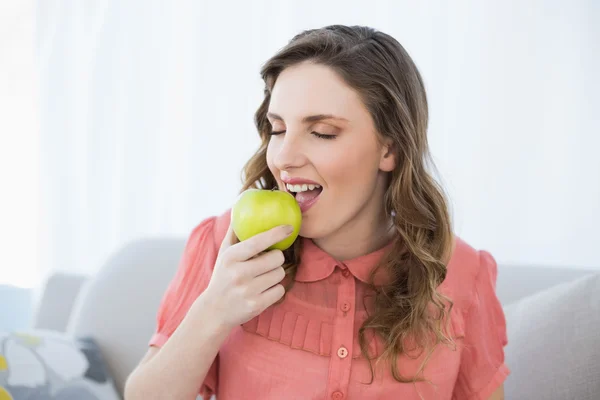 Enjoying pregnant woman eating green apple sitting on couch — Stock Photo, Image