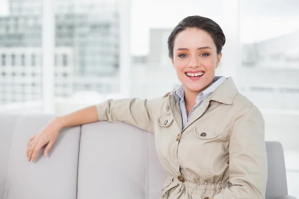 Uśmiechający się dobrze ubrany, młoda kobieta siedzi na kanapie — Zdjęcie stockowe