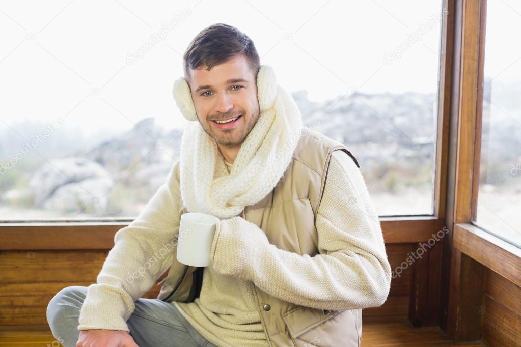 Smiling man wearing earmuff with coffee cup against window