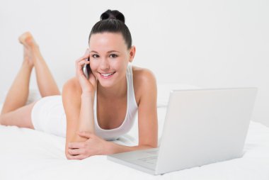 gülümseyen casual kadın yatakta kullanarak cep telefonu ve laptop