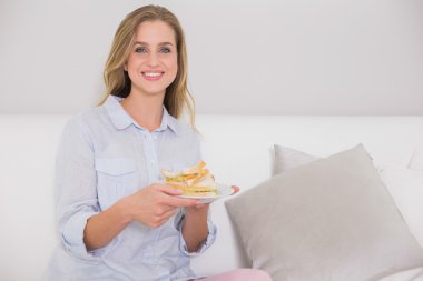 sandviç tutarak kanepede oturan mutlu rahat sarışın