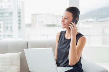 güzel iyi giyimli kadın kanepede dizüstü bilgisayar ve cep telefonu kullanma