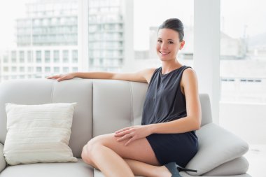 evde bir kanepede oturan kadın giyinmiş de gülümseyerek