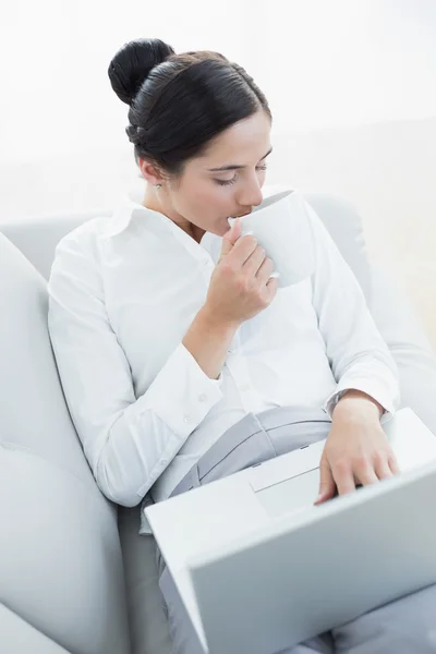 Mujer bien vestida bebiendo café mientras usa computadora portátil y café — Foto de Stock