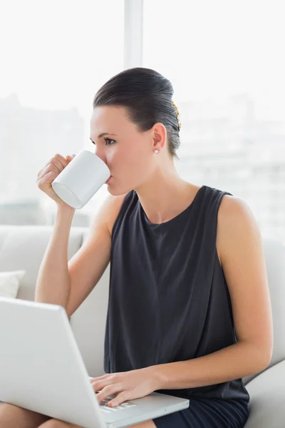Hermosa mujer bien vestida usando el ordenador portátil mientras bebe café — Foto de Stock