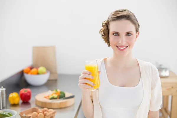 Mulher bonita posando em sua cozinha segurando um copo de laranja — Fotografia de Stock