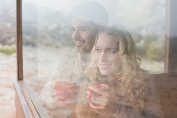 Thoughtful content couple with cups looking through window — Stock Photo, Image