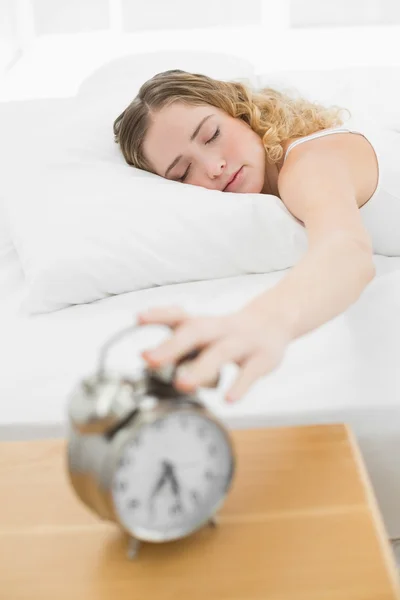 Ziemlich zufriedene Blondine liegt im Bett und schaltet den Wecker aus — Stockfoto