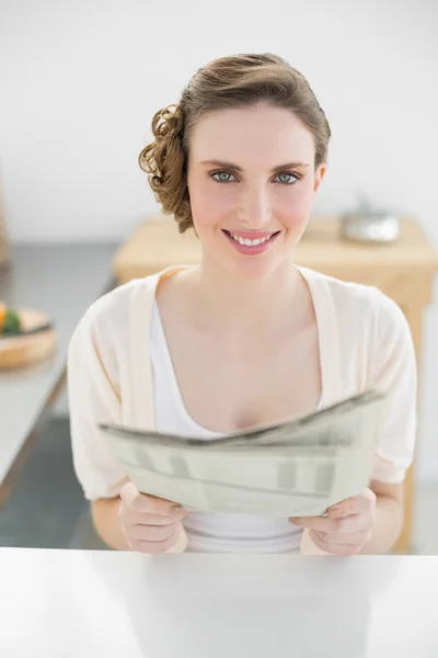 Hermosa mujer tranquila sosteniendo periódico sentado en su cocina — Foto de Stock