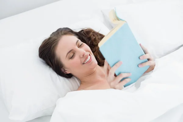 Lachende vrouw lezen van een boek in bed — Stockfoto