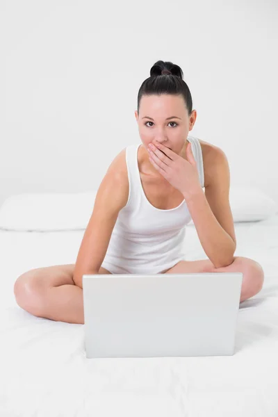 Shocked casual woman using laptop in bed — Stock Photo, Image