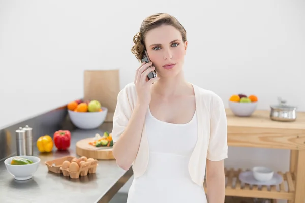 Young woman standing in kitchen while phoning — Stock Photo, Image