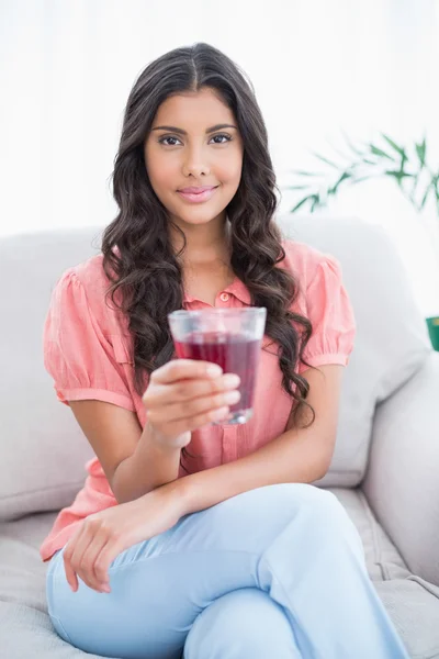 Zawartość ładny brunetka siedzi na kanapie, trzymając szklankę soku — Zdjęcie stockowe