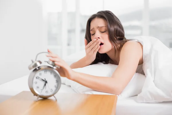 Frau gähnt, während sie Zeiger auf Wecker ausstreckt — Stockfoto