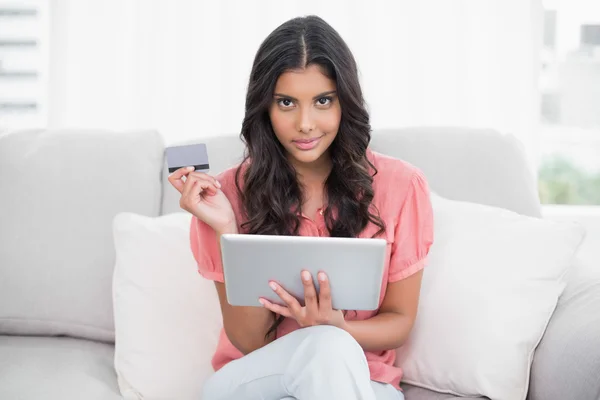 Calma morena bonito sentado no sofá segurando cartão de crédito e tablet — Fotografia de Stock