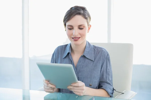 Sorrindo jovem empresária sentada em sua mesa segurando um tablet — Fotografia de Stock