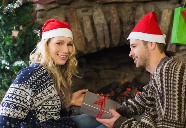 Man gifting woman in front of lit fireplace during Christmas — Stock Photo, Image