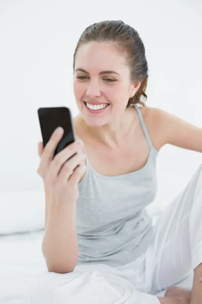 Улыбающаяся женщина смотрит на мобильный телефон в постели — стоковое фото