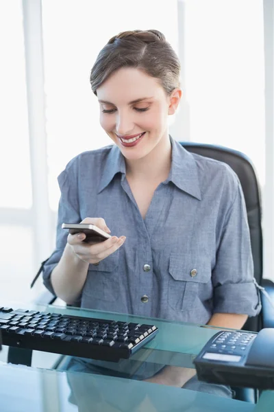 Zufriedene Geschäftsfrau sitzt mit Smartphone am Schreibtisch — Stockfoto