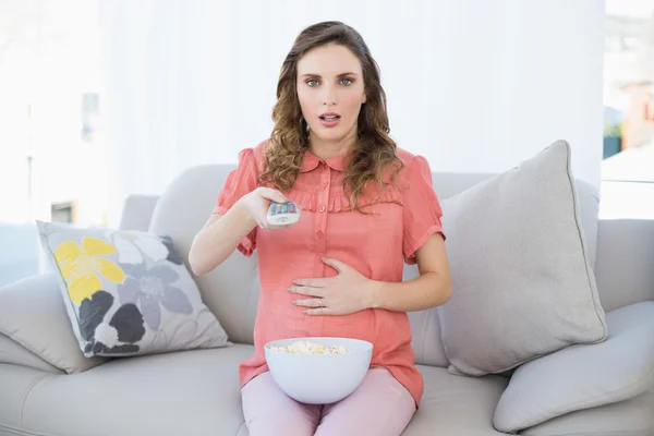 Förvånad gravid kvinna sitter i vardagsrummet framför TV hemma — Stockfoto