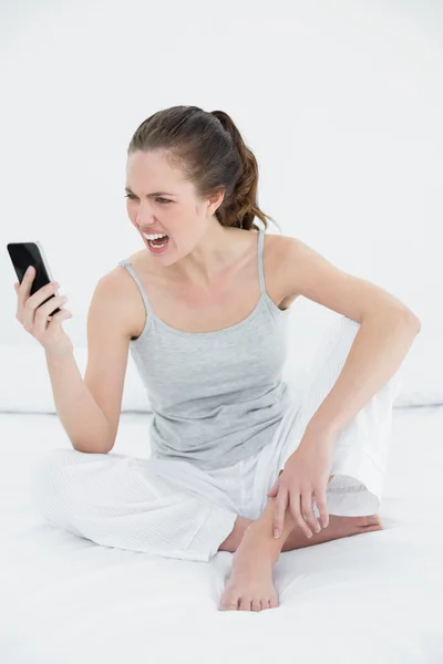 Женщина кричит в мобильный телефон в постели — стоковое фото
