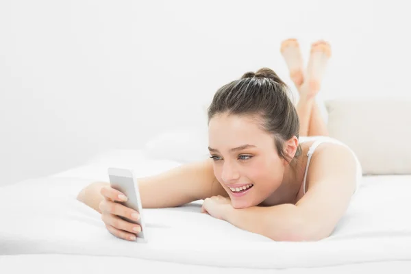Felice donna casual guardando il telefono cellulare a letto — Foto Stock