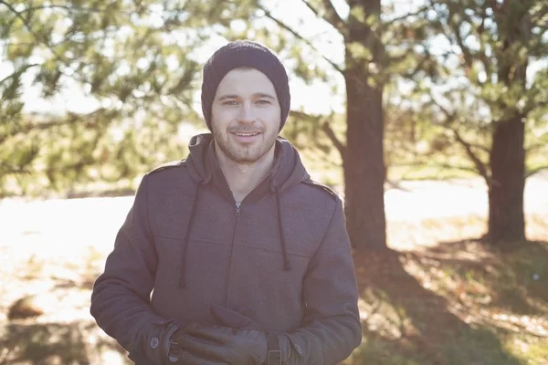Smiling young man in warm clothing in forest — Stock Photo, Image
