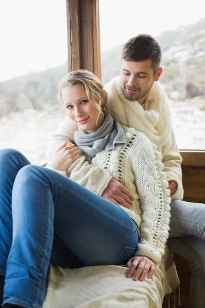 Couple in winter clothing sitting against window — Stock Photo, Image