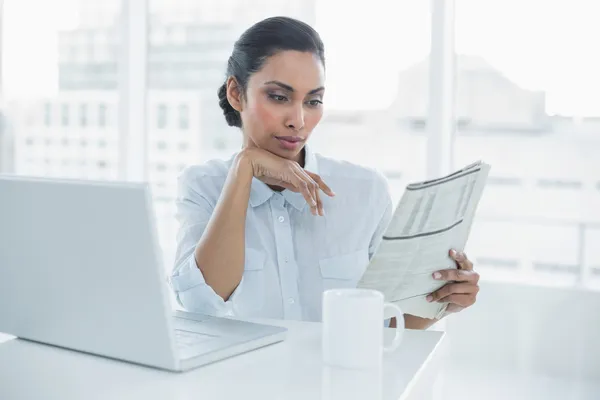 Mujer de negocios seria leyendo el periódico sentado en su escritorio —  Fotos de Stock