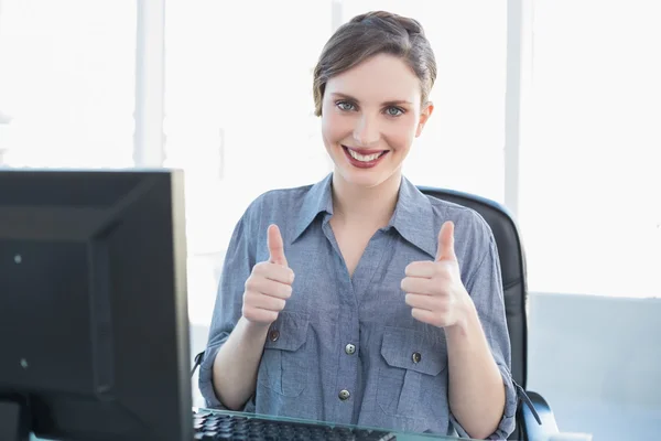 Vrolijke zakenvrouw tonen duimschroef opwaarts zit op haar Bureau — Stockfoto