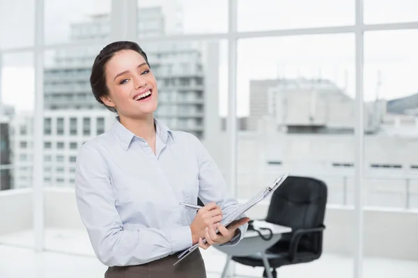 Empresária elegante alegre com prancheta no escritório — Fotografia de Stock