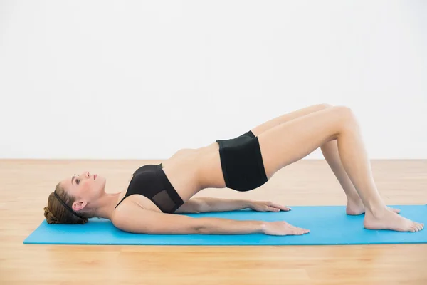 Focused sporty woman lying on blue exercise mat doing exercises — Stock Photo, Image