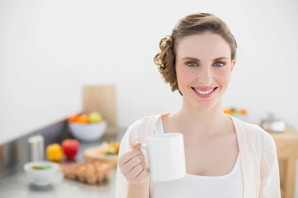 Mujer joven sonriente posando en la cocina sosteniendo una taza —  Fotos de Stock