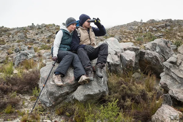Couple sitting on rock with binoculars while on a hike — Stock Photo, Image