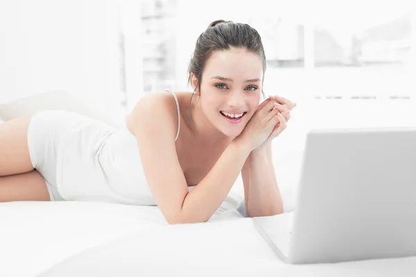 微笑与躺在床上的笔记本电脑随便的女人 — 图库照片