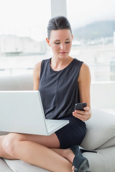 Mulher bonita bem vestida usando laptop e celular no sofá — Fotografia de Stock