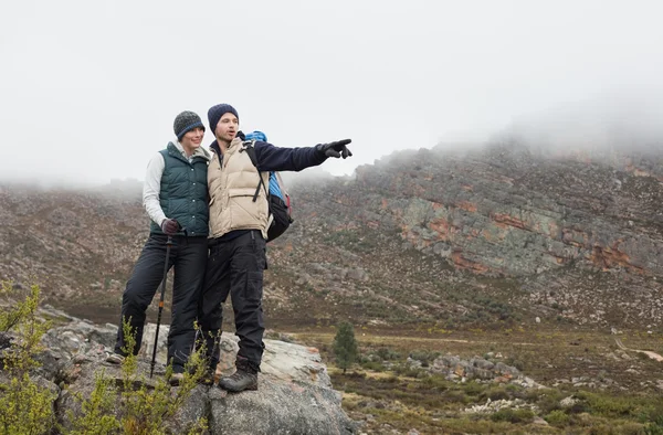 Casal de pé em uma rocha olhando para as montanhas — Fotografia de Stock