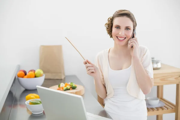 Lächelnde schöne Frau telefoniert, während sie in der Küche steht — Stockfoto