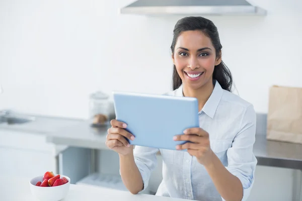 Mujer joven encantadora sosteniendo su tableta de pie en la cocina brillante —  Fotos de Stock