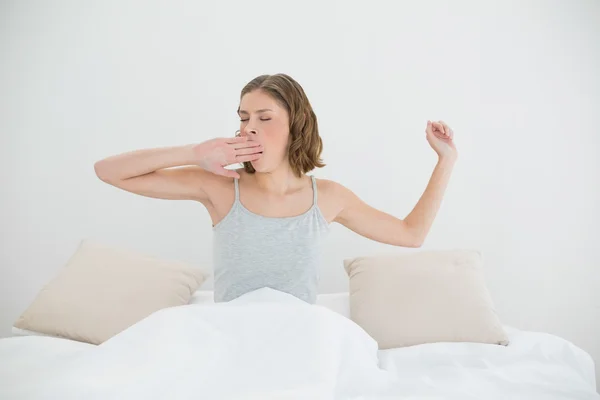 Mulher bonita esticando e bocejando sentado em sua cama — Fotografia de Stock